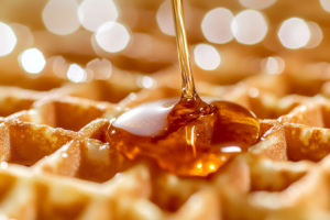 A close-up image of perfectly cooked golden brown waffles topped with melted butter and syrup, highlighting the texture and crispiness of the waffles. 